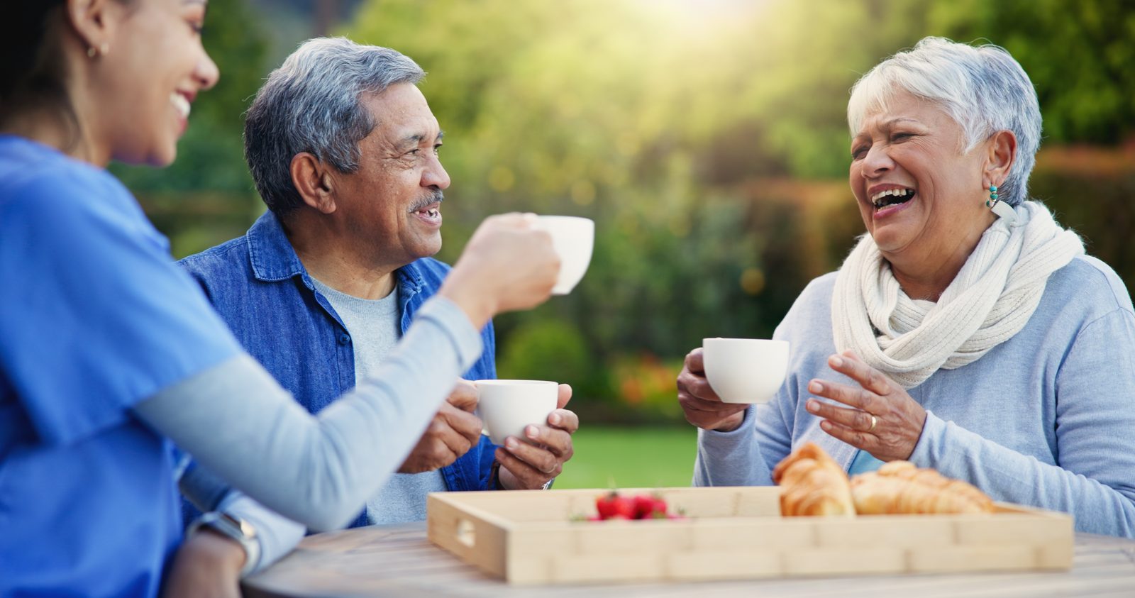 A caregiver sharing coffee with two seniors in the garden
