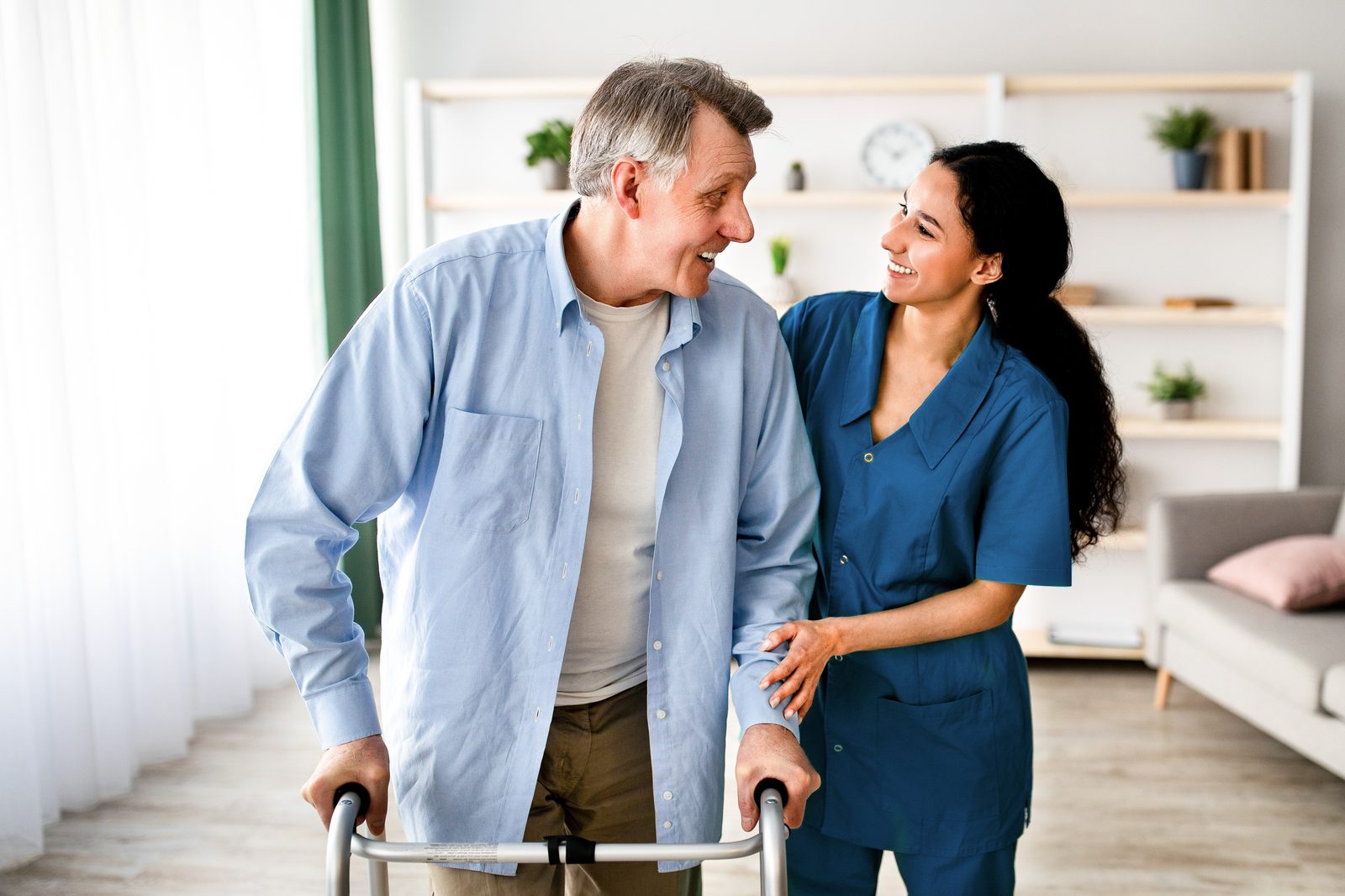 A caregiver helping a senior man walk with his walker at home
